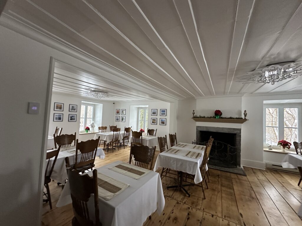 Salle à manger de l’Auberge du Manoir avec tables nappées et cheminée.