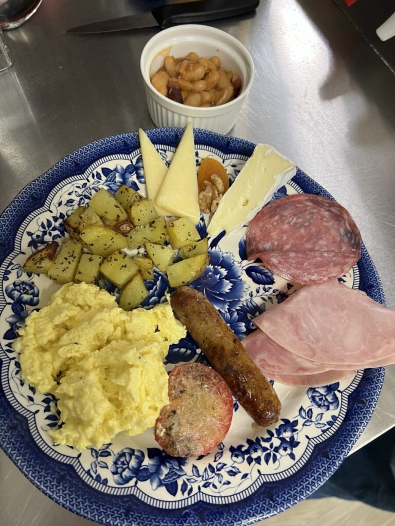 Assiette de déjeuner avec œufs, pommes de terre, charcuteries et accompagnements.